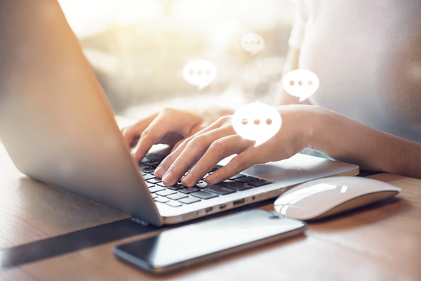 A person typing on a computer with chat bubbles 