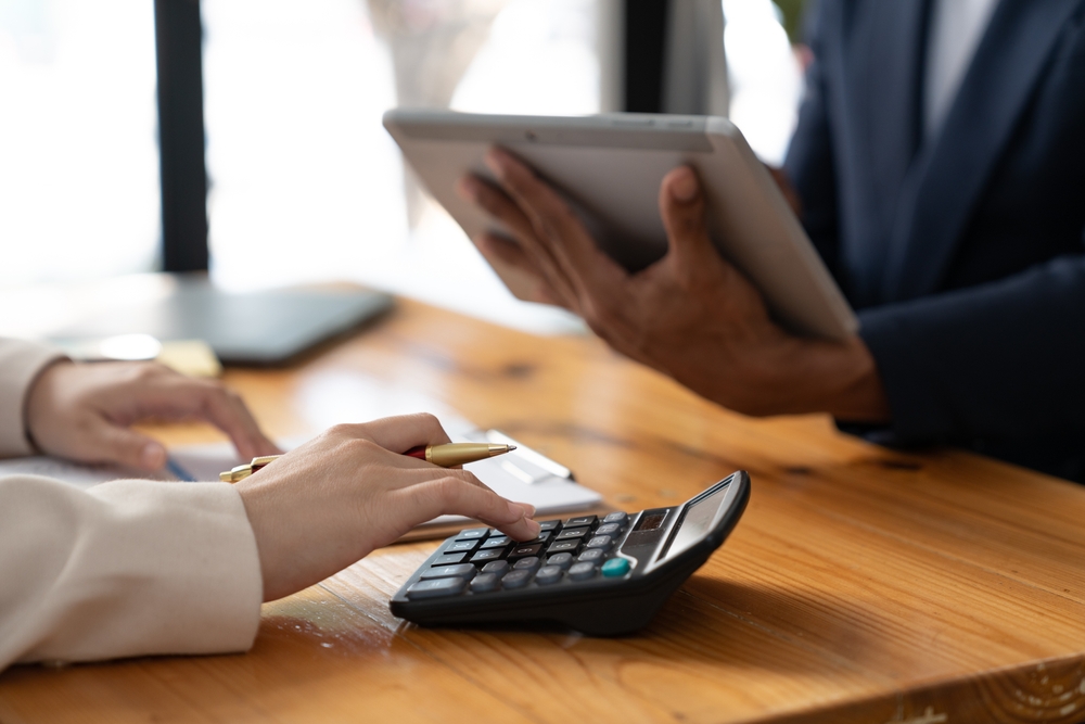 A person holding an Ipad and another person working with a calculator 